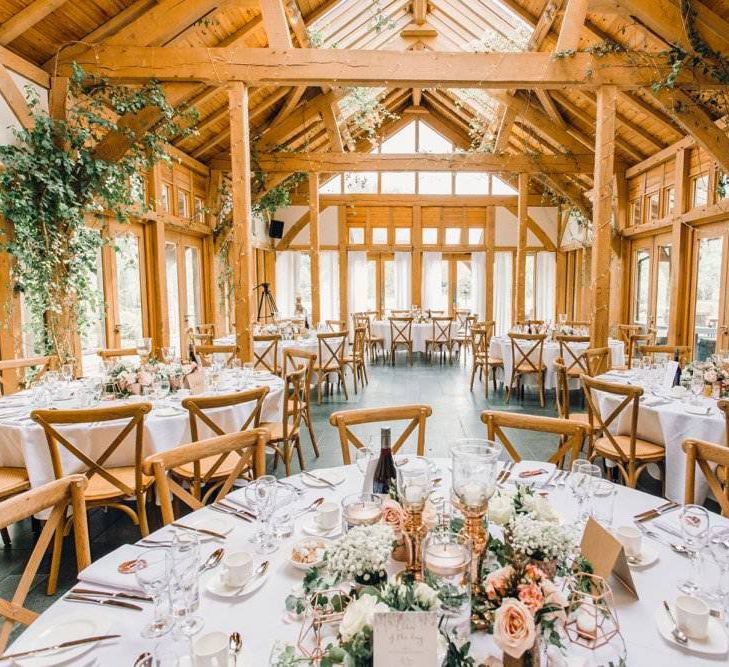 Rustic styled wedding reception with beams decorated in green foliage and gypsophila bouquets