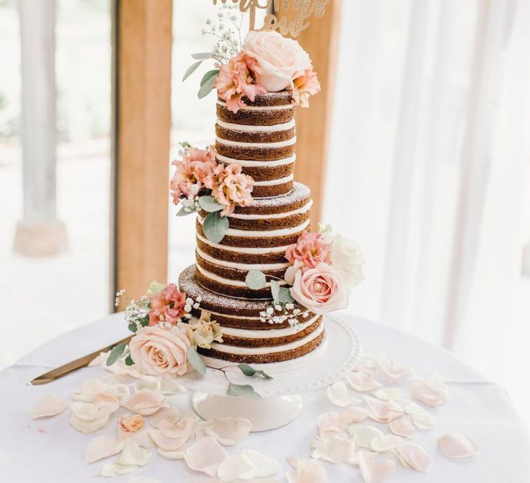 Naked wedding cake with pink rose decor and a personalised gold cake topper