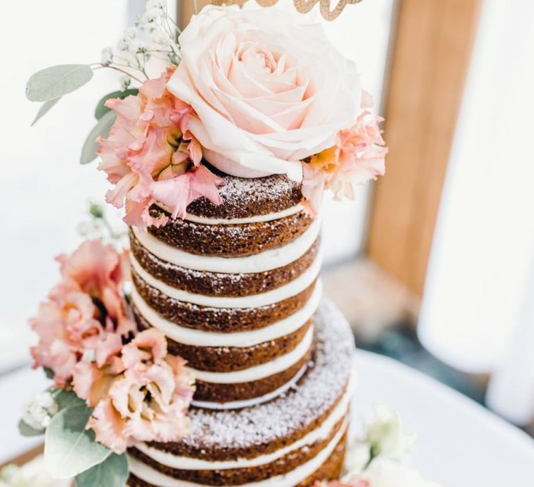 Naked three tier wedding cake with pink roses and a gold cake topper