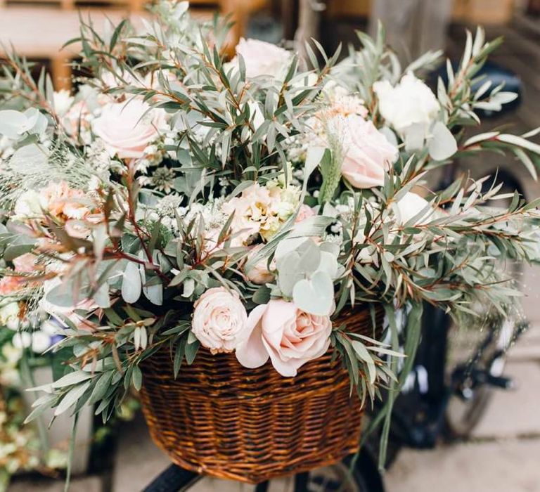 Beautiful pink rose flower arrangements in the basket of a rustic wedding bike sign