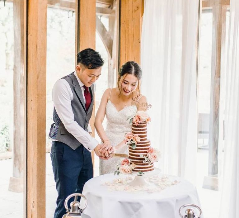 Bride and groom cut the naked wedding cake with dusky pink rose detailing and tall candle lanterns