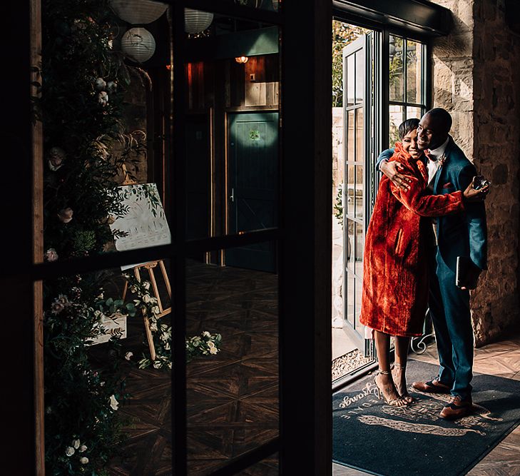 Groom embracing a wedding guests in red faux fur coat