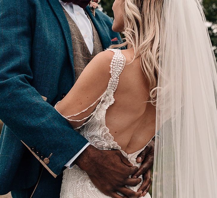 Groom embracing his bride in a lace, low back wedding dress and veil