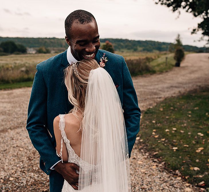 Groom in blue blazer embracing his bride in a lace wedding dress