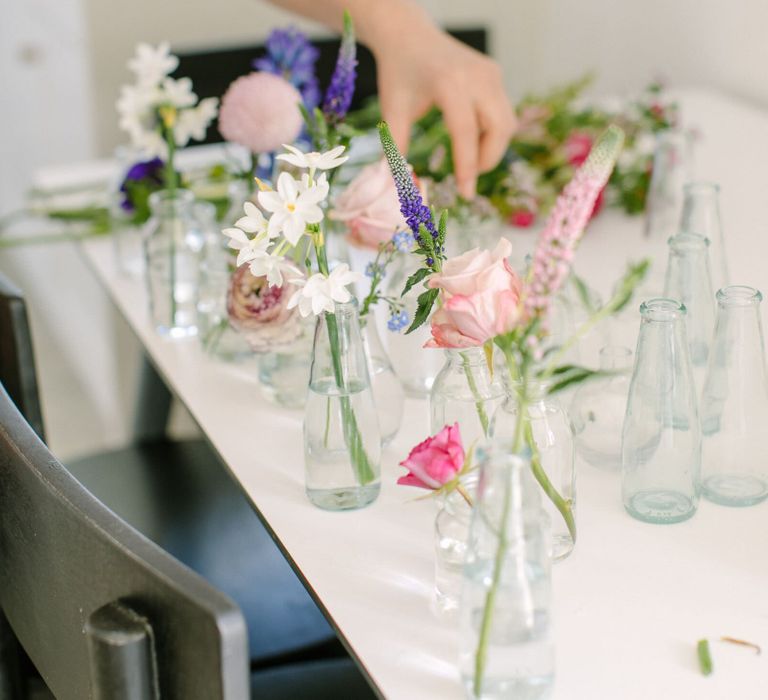 Person arranging single stems of flowers in glass vases and milk bottles to create a wedding centrepiece