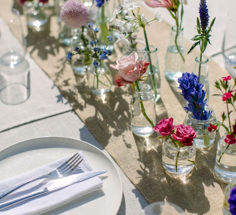 Wedding centrepiece created using single stems of vibrant pink, purple and blue spring flowers in glass bottles