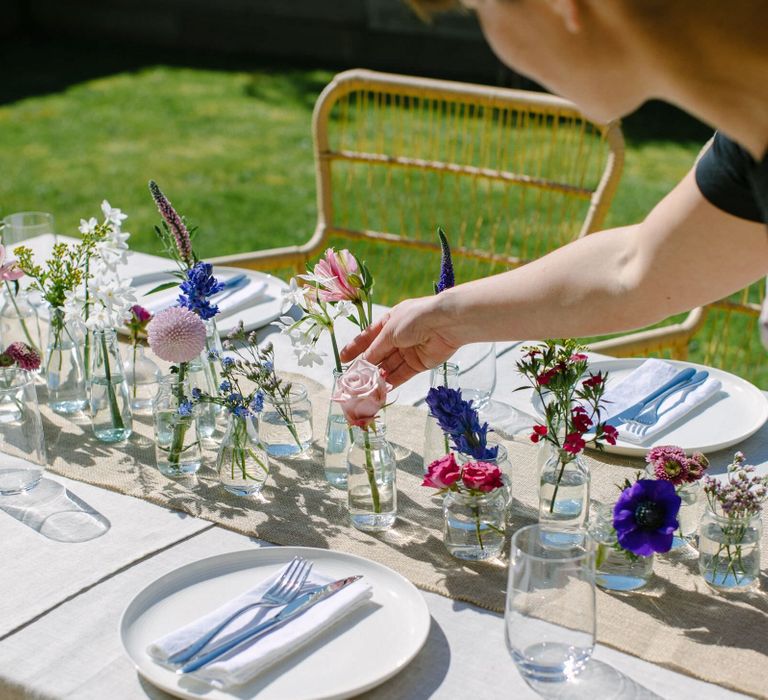 Person creating a floral centrepiece using pale pink roses, purple anemones and blue hyacinths