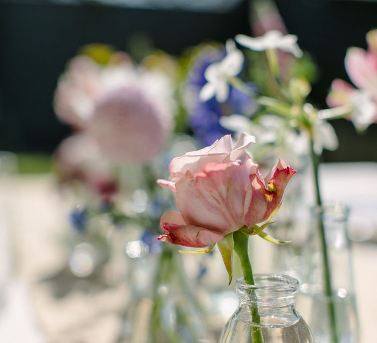 Close up of a single pale pink antique rose in a mini glass milk bottle vase as part of a wedding centrepiece