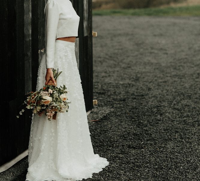 Stylish bride in sequin skirt and bridal crop top with flower crown and bouquet