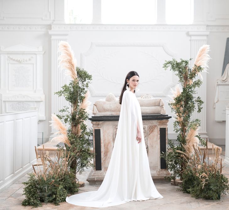 Bride in Plain Bridal Cape Standing in Front of a Floral installation of Pampas Grass and Dried Flowers