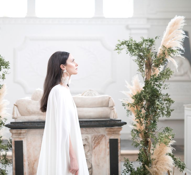 Bride Wearing Statement Earrings and Plain Bridal Cape Standing in Next to  Floral Installation of Pampas Grass and Dried Flowers