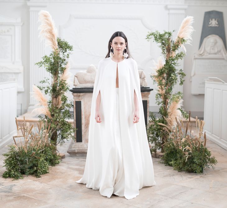 Stylish Bride in Jesus Peiro Wedding Dress and Bridal Cape Standing in Next to a Floral installation of Pampas Grass and Dried Flowers