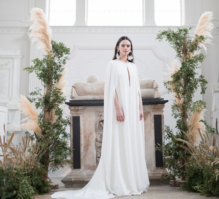 Stylish Bride in Jesus Peiro Plain Bridal Cape Standing in Next to a Floral installation of Pampas Grass and Dried Flowers