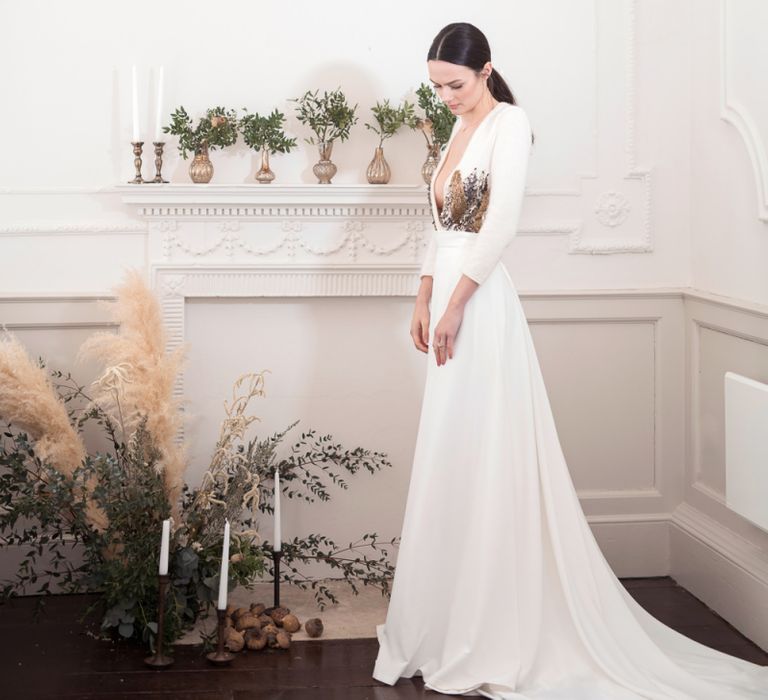 Bride in Jesus Peiro Wedding Dress with Plunging Neckline Standing Next to a Fireplace