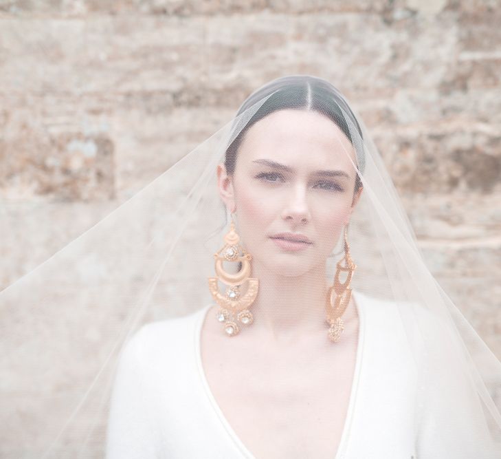 Beautiful Bride with Natural Makeup in Sheer Bridal Veil Showing off Statement Earrings and Sleek Hairstyle