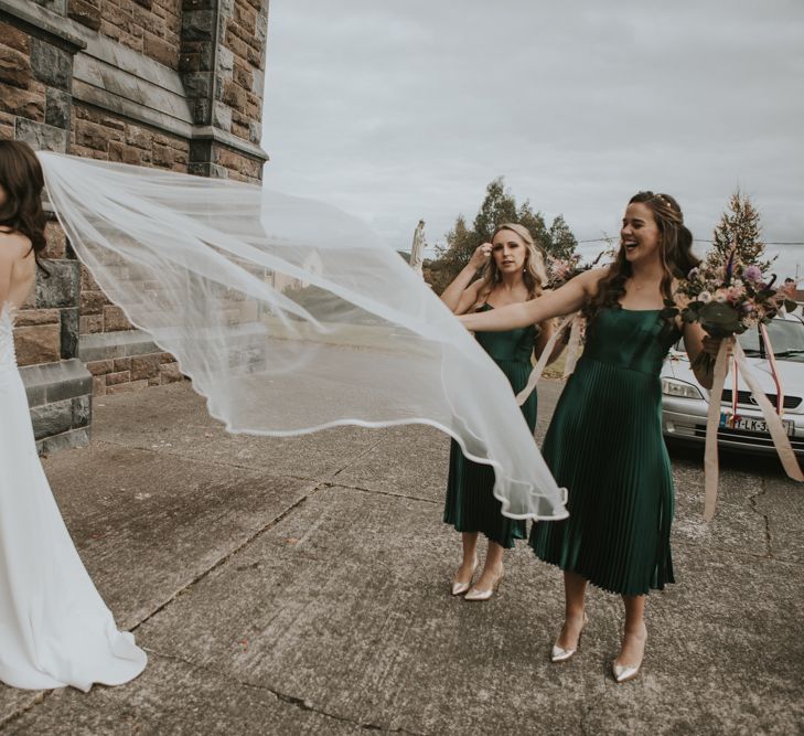 Bridal Party with Bride in High Low Elbeth Gillis Wedding Dress and Veil and Bridesmaids in Pleated Skirt Emerald Green Dresses