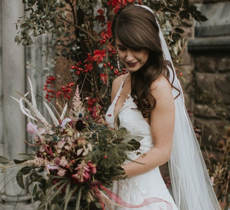 Bride in Elbeth Gillis Wedding Dress Holding a Deep Red and Green Wedding Bouquet