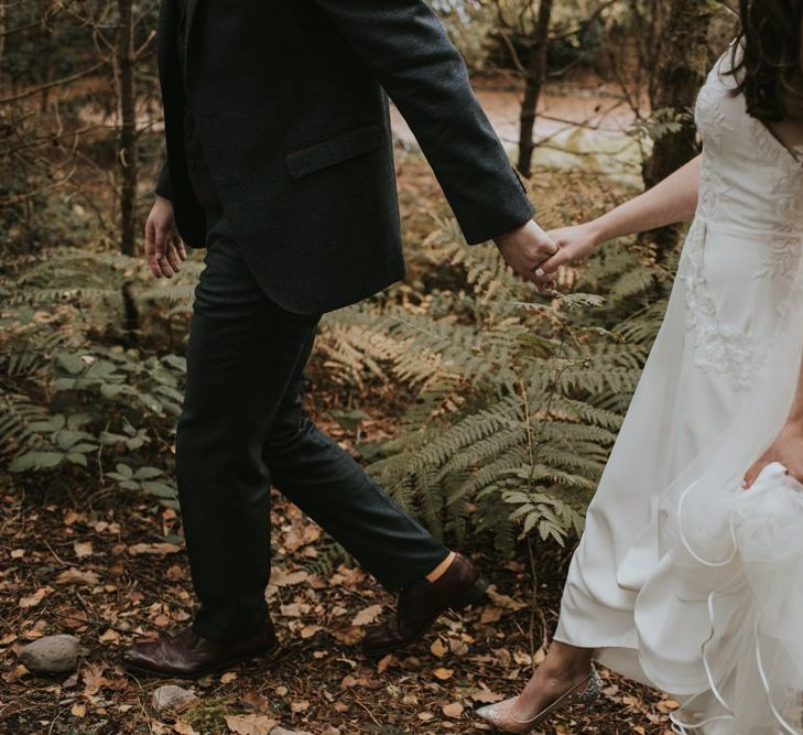 Bride in Elbeth Gillis Wedding Dress and Groom in  Tweed Suit  Hand in Hand Through The Woods