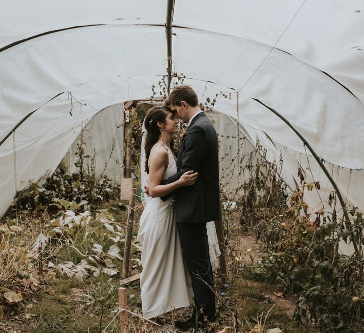 Bride in Elbeth Gillis Wedding Dress and Groom in  Tweed Suit  Embracing in a Greenhouse