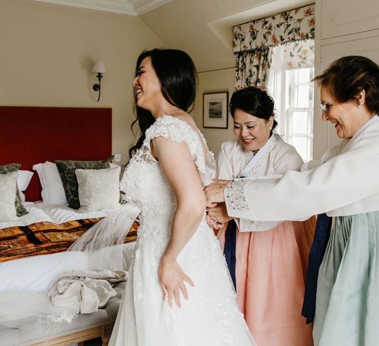 Mother of the bride and groom helping the bride into her wedding dress