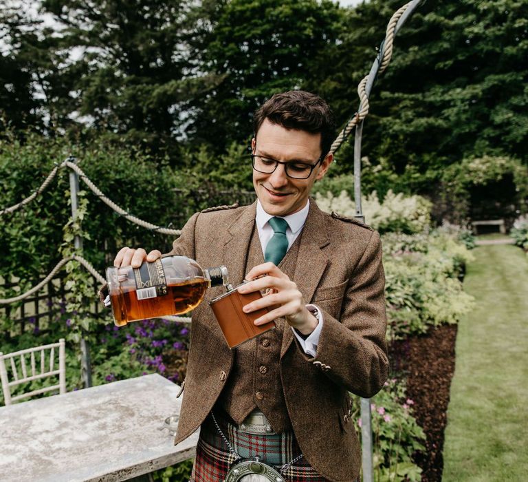 Scottish groom in kilt drinking whiskey on wedding morning