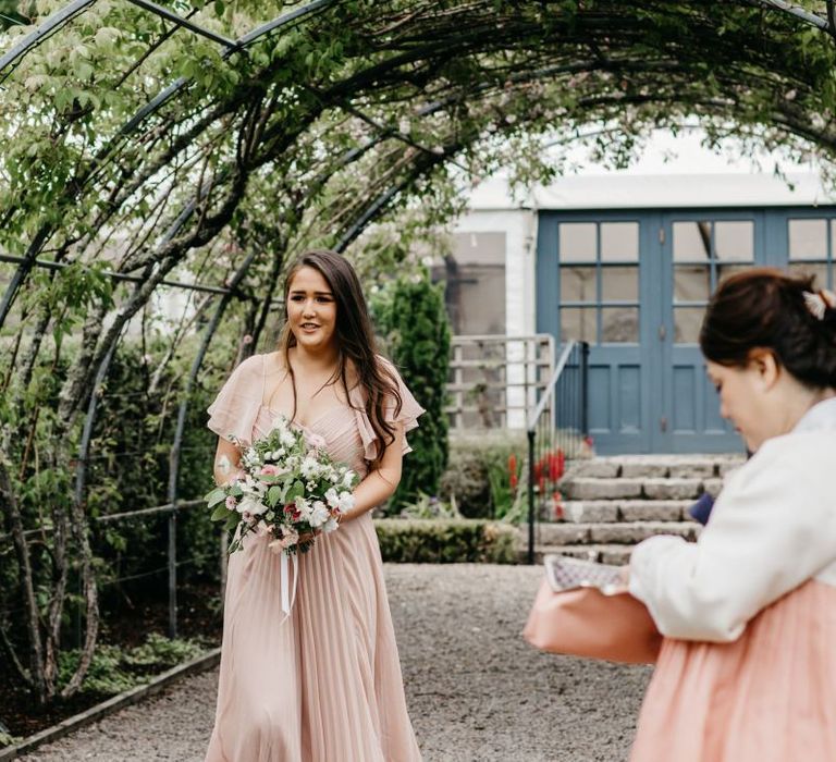 Bridesmaids in dusky pink dress walking down the aisle