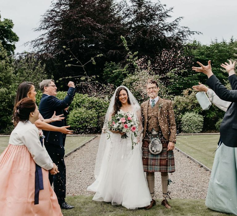 Confetti moment with bride in lace and tulle dress, groom in tartan kilt and parents in Hanboks - Korean wedding dress