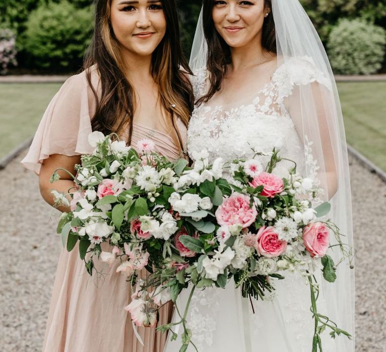 Bride in lace and tulle wedding dress with her bridesmaid in a pink dress