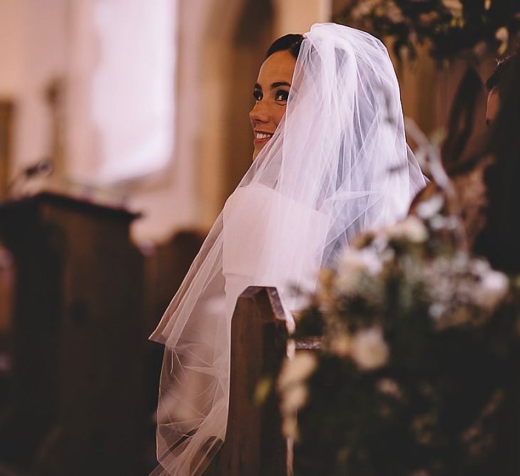 Bride with white rose bouquet at church ceremony with long statement veil