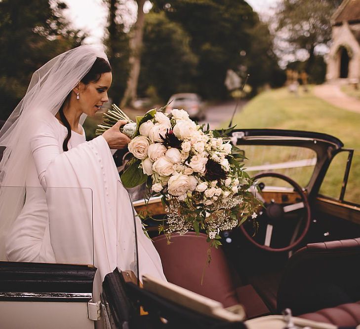 Bride and groom travel in style to the reception holding white rose bouquet