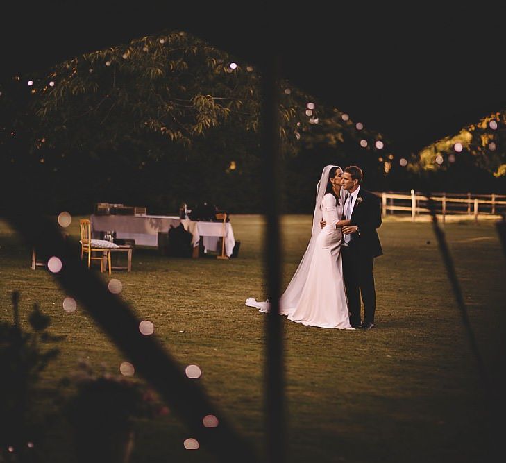 Bride and groom embrace at garden party tipi reception with fairy light decor