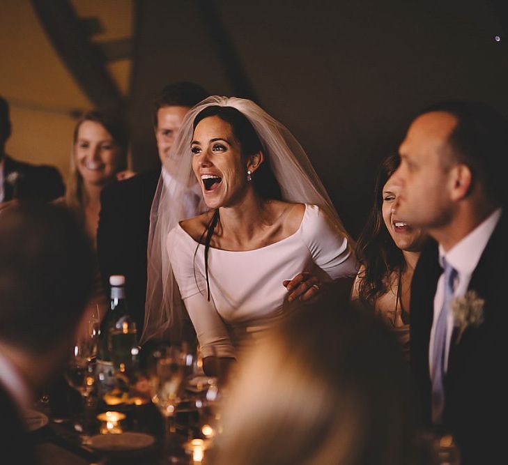 Bride and groom enjoy the wedding speeches at tipi reception with rustic styling