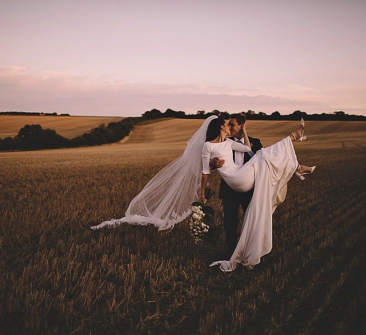 Bride and groom steal a moment for epic sunset wedding shot holding white rose bouquet