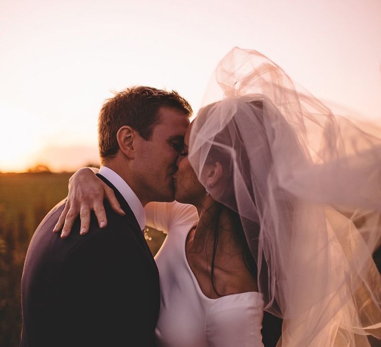 Bride and groom steal a moment for epic sunset wedding shot holding white rose bouquet