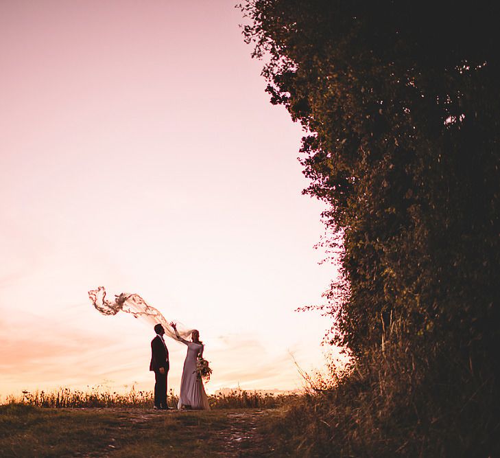 Bride and groom steal a moment for epic sunset wedding shot holding white rose bouquet