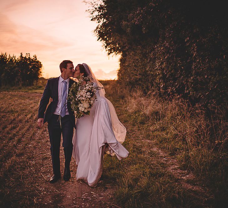 Bride and groom steal a moment for epic sunset wedding shot holding white rose bouquet