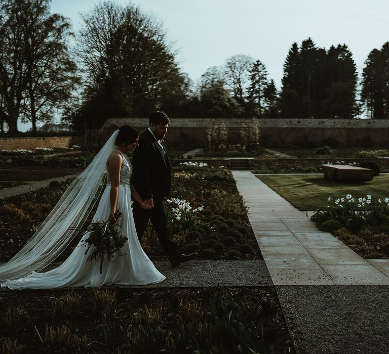 Bride in Maggie Sottero Wedding Dress and Groom in Dark Suit Walking through Middleton Lodge Gardens