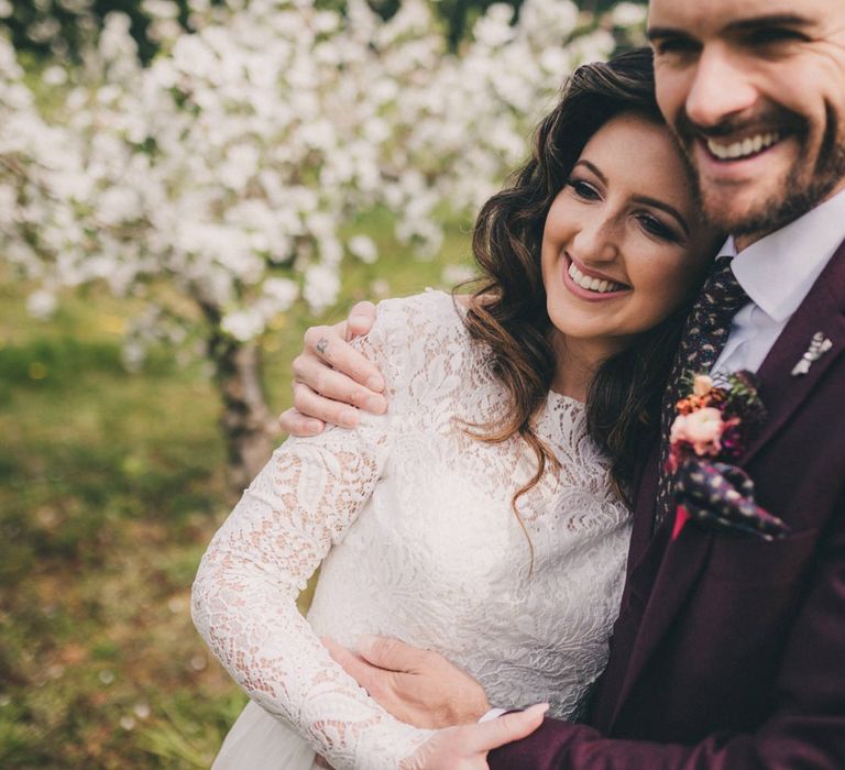 Groom in Burgundy Suit and Bride in Lace Wedding Dress Embracing