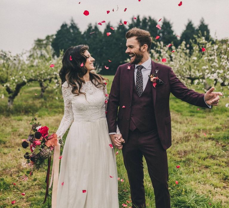 Red Confetti Moment with Bride in Lace Wedding Dress and Groom in Burgundy Suit