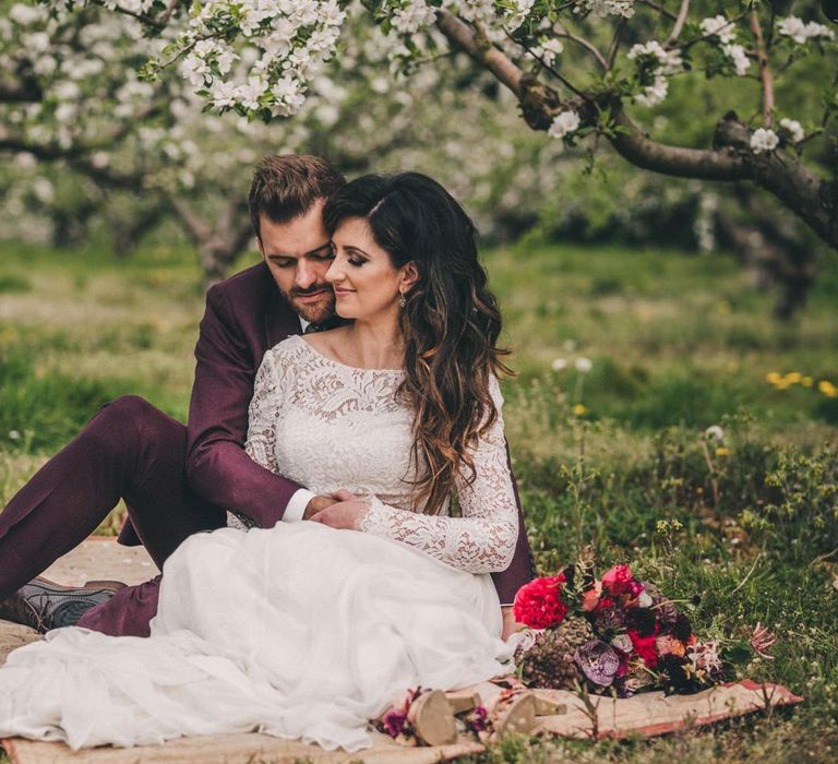 Bride and Groom Embracing on a Rug in an Orchard