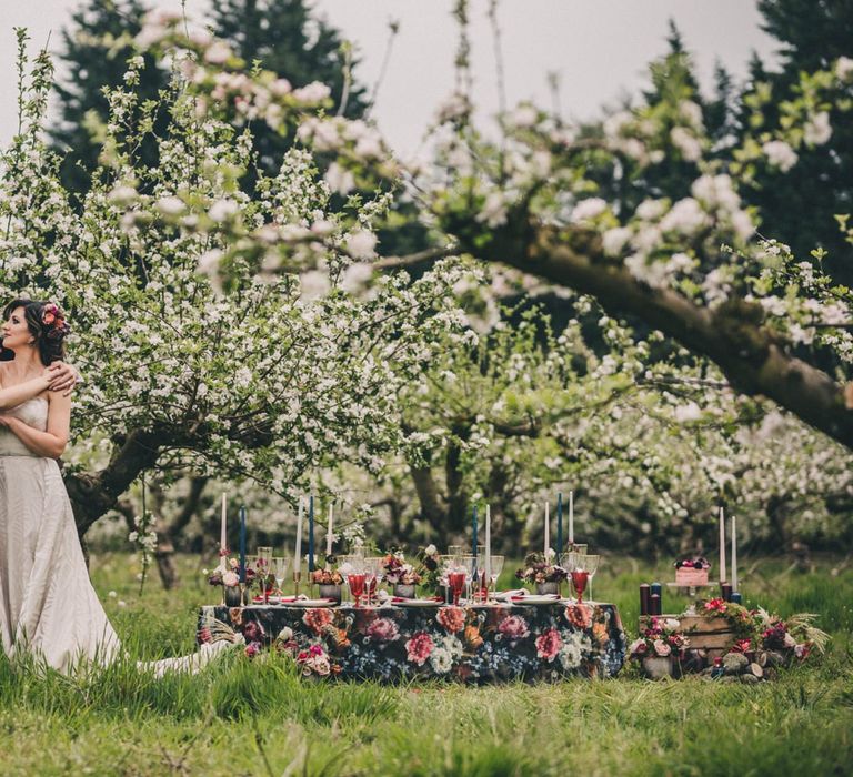 Groom in Black Tie Suit and Bride in Off the Shoulder Dress Standing in an Orchard