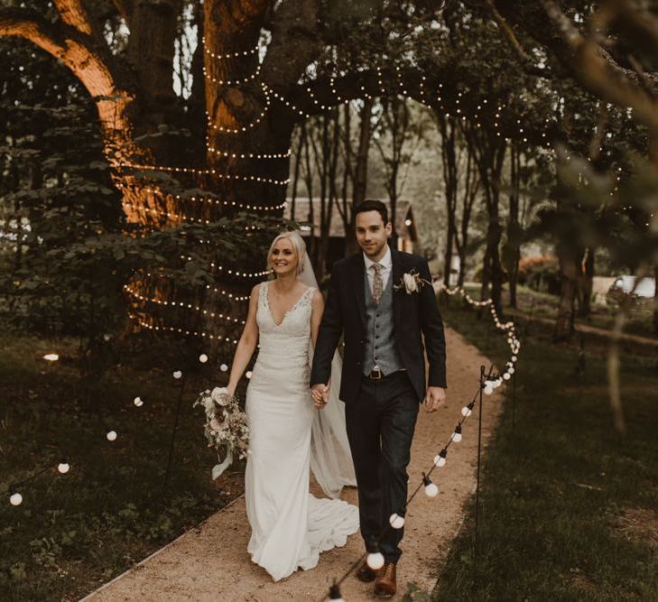 Bride and groom walk down pathway lit by fairy lights