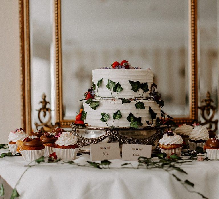 White wedding cake with foliage decor with cupcakes surrounding