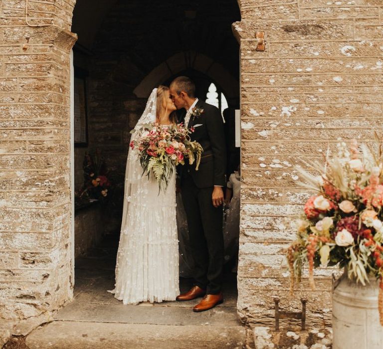 Bride in Eliza Jane Howell wedding dress kisses groom outside church