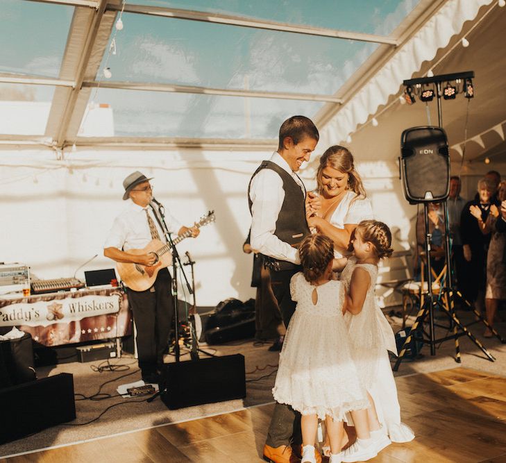 Bride in Eliza Jane Howell wedding dress and groom with their daughters dancing