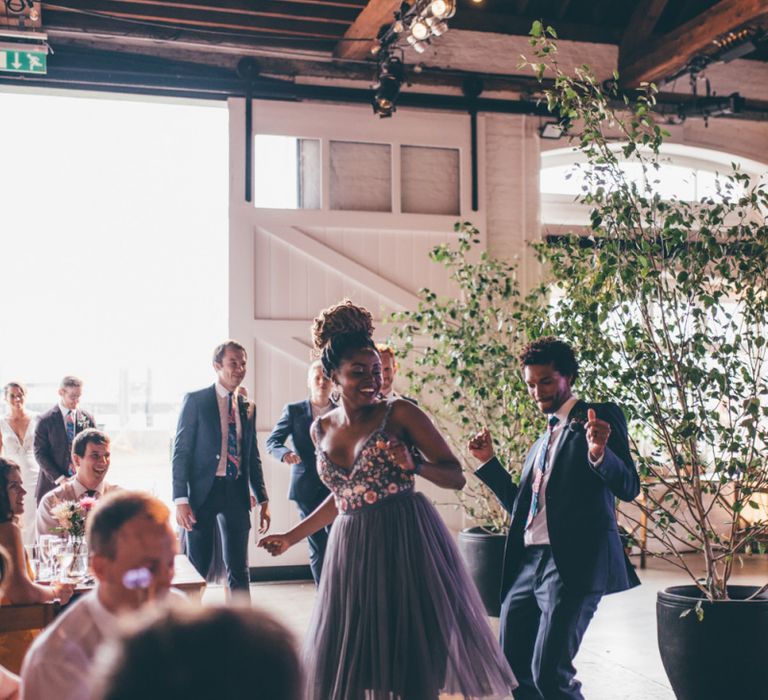 Wedding guests celebrate and industrial styled venue with fairy light backdrop in London