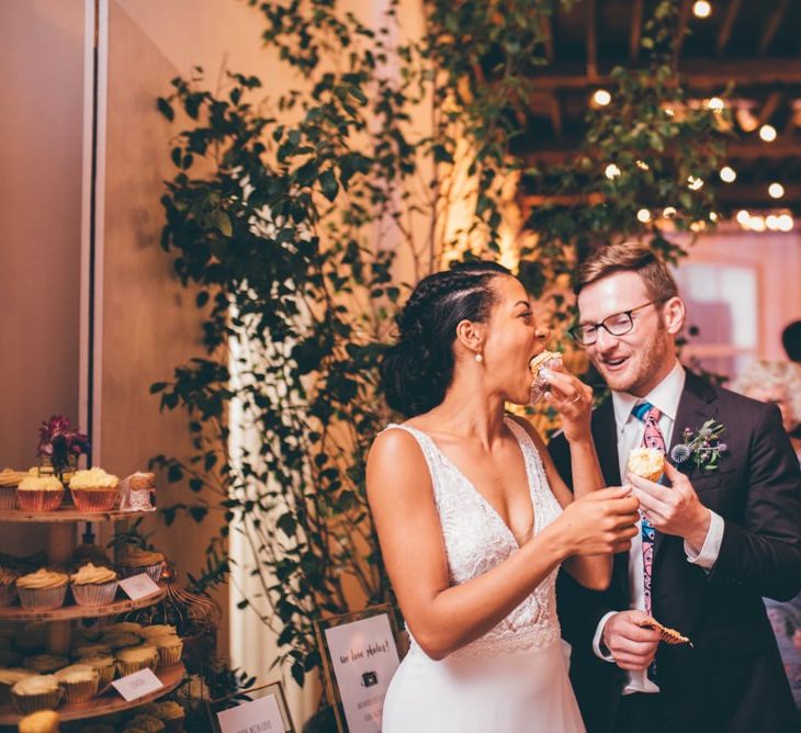 Bride and groom enjoying the cupcake wedding cake tower with fairy light backdrop