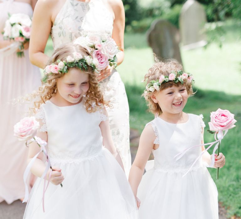 Flower girls in white dresses holding a pink flower stem and flower crown