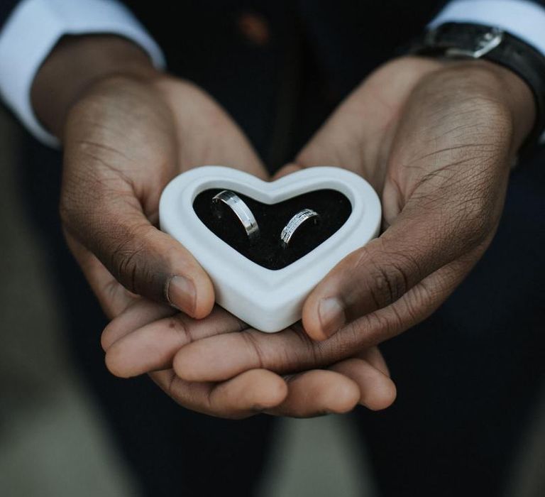 Groom holding heart ring box with wedding bands