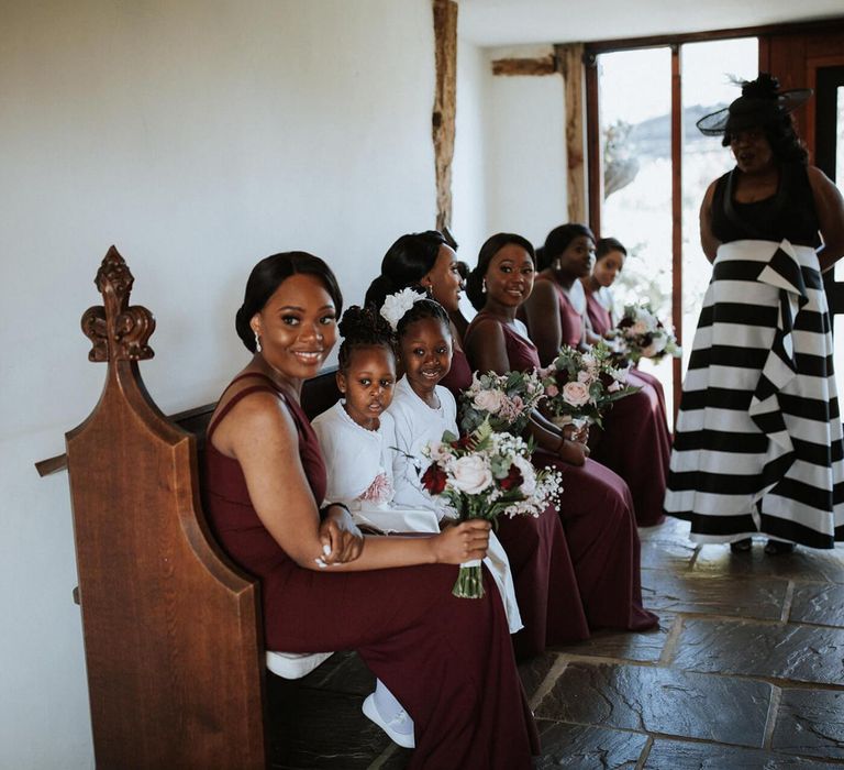 Bridesmaids in burgundy dresses sitting on a bench